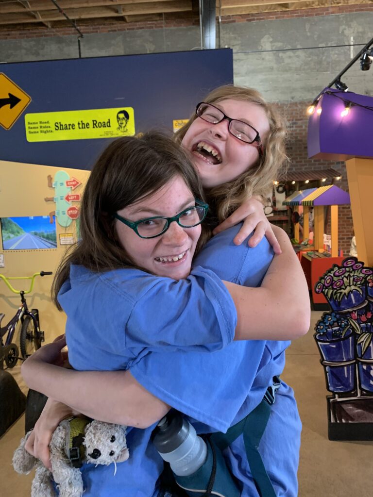 Two young girls in blue shirts hugging.